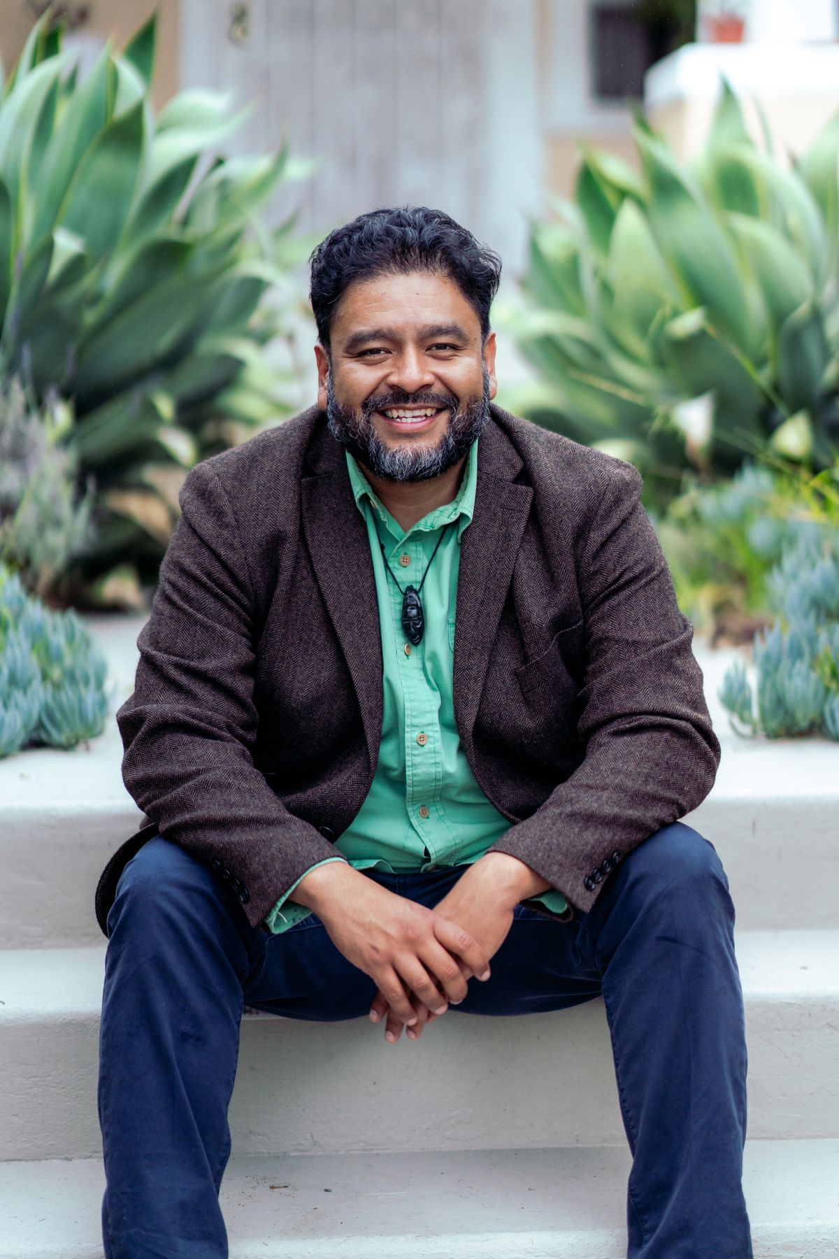 Estuardo Mazariegos, smiling, seated on front steps in a South Los Angeles garden